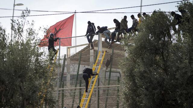 FILE PHOTO: African migrants sit on top of a border fence during an attempt to cross into Spanish territories, between Morocco and Spain's north African enclave of Melilla