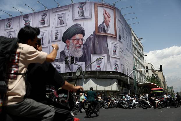 People ride motorcycles near a billboard featuring an image of the late Supreme Leader of Iran, Ayatollah Ali Khamenei, in Tehran