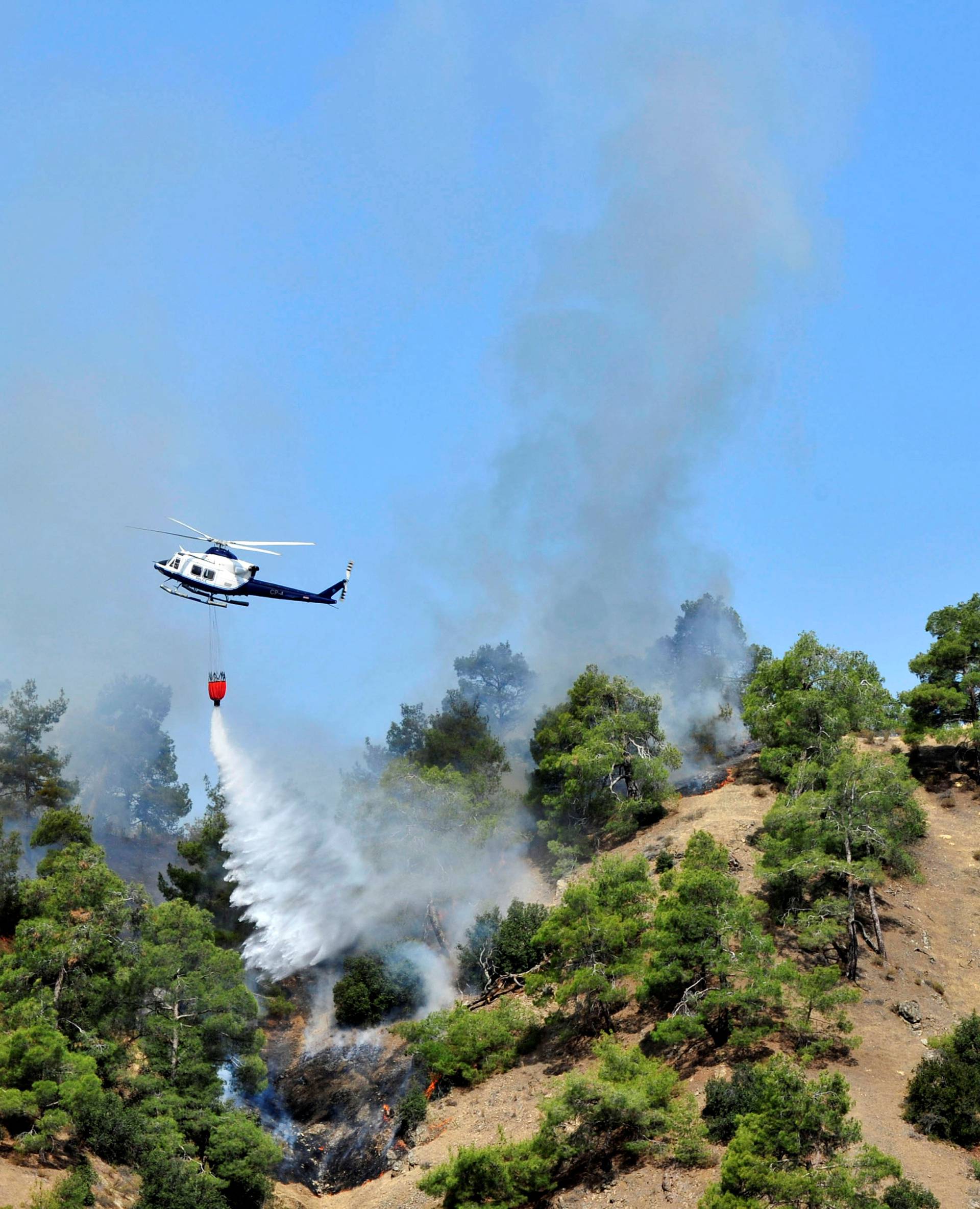 A firefighting helicopter drops water onto a forest fire at the foothills of Troodos mountain region in Cyprus
