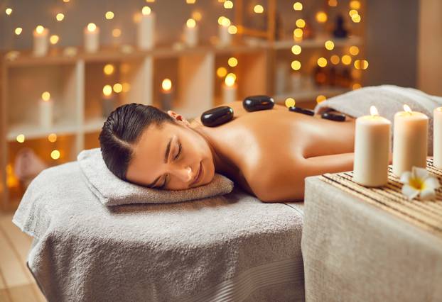 Beautiful young woman getting massage at a spa salon with stones.