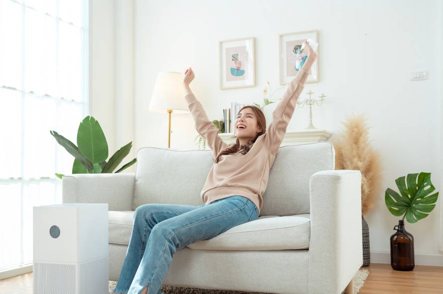 A,Woman,Sits,On,A,Couch,,Operating,An,Air,Purifier