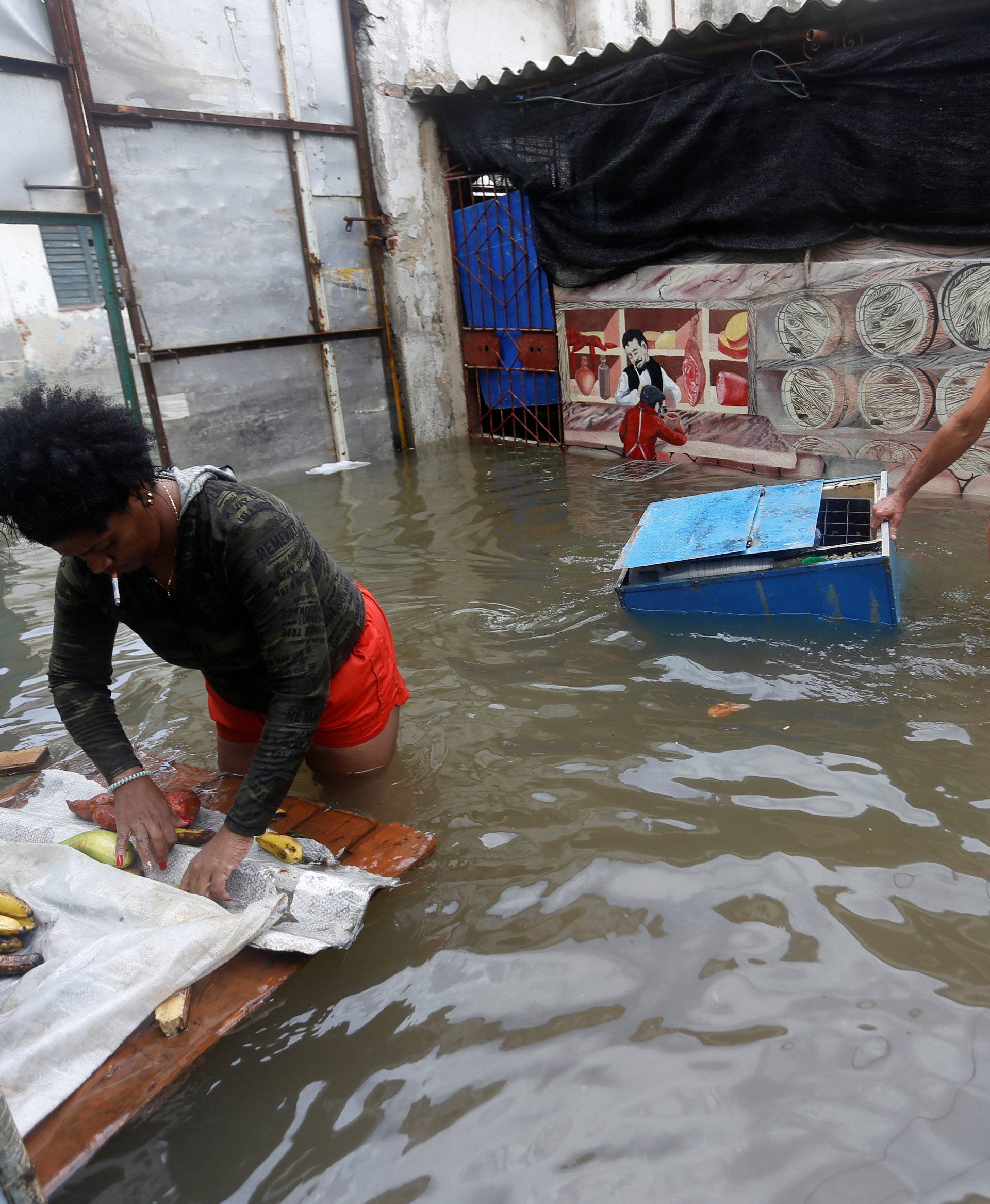 A woman rolls produce into a bag as a man drags a cooler through the water, after the passing of Hurricane Irma, in Havana