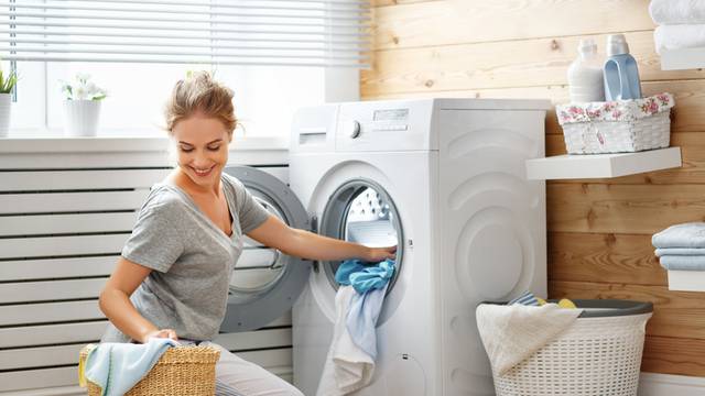 Happy housewife woman in laundry room with washing machine  