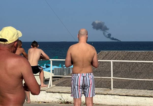 People look at a ship burning at sea in Odesa