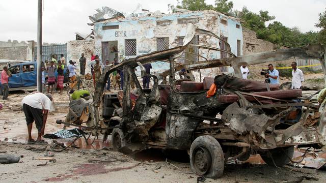 Civilians remove the body of an unidentified man from the wreckage of a minibus at the scene of an explosion near  a military base in Somalia's capital Mogadishu