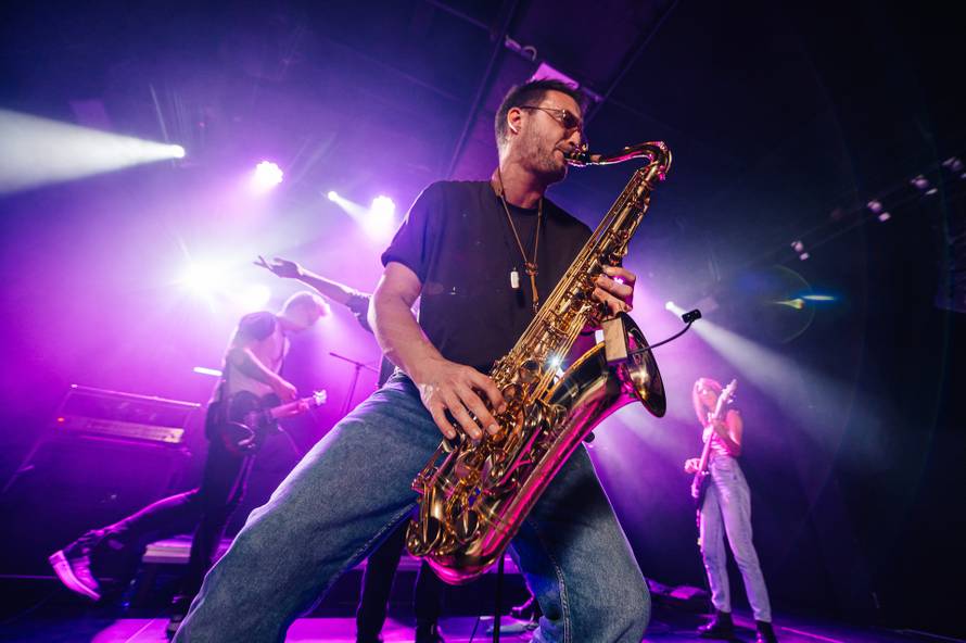 Saxophonist,Playing,Saxophone,Solo,With,Band,Members,Performing,On,Stage