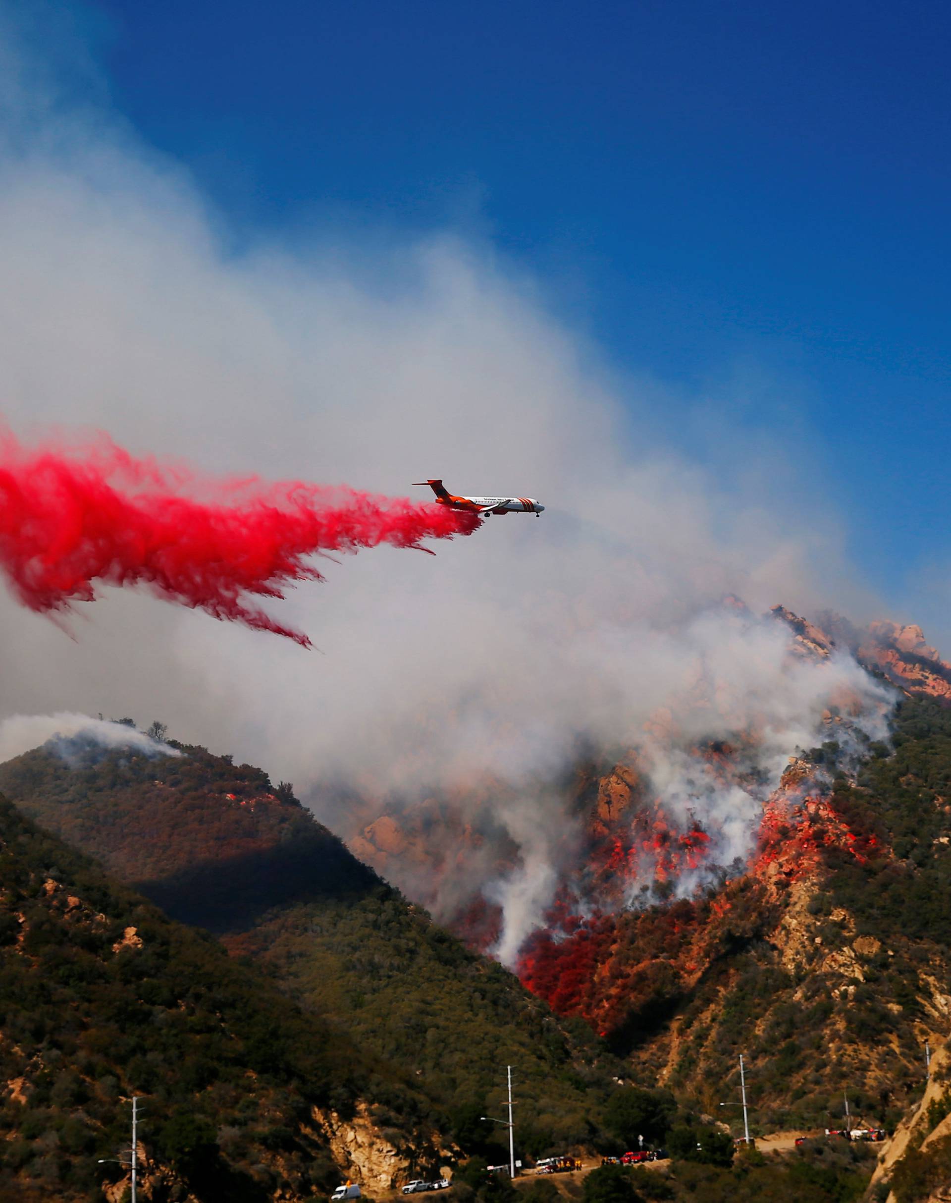 An aircraft drops flame retardant as firefighters battle the Woolsey Fire as it continues to burn in Malibu