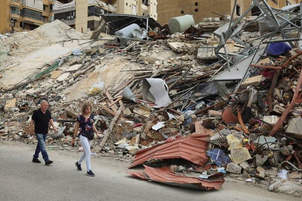 A couple walks past a damaged building, after a 10-day ceasefire between Lebanon and Israel went into effect, in the southern suburbs of Beirut