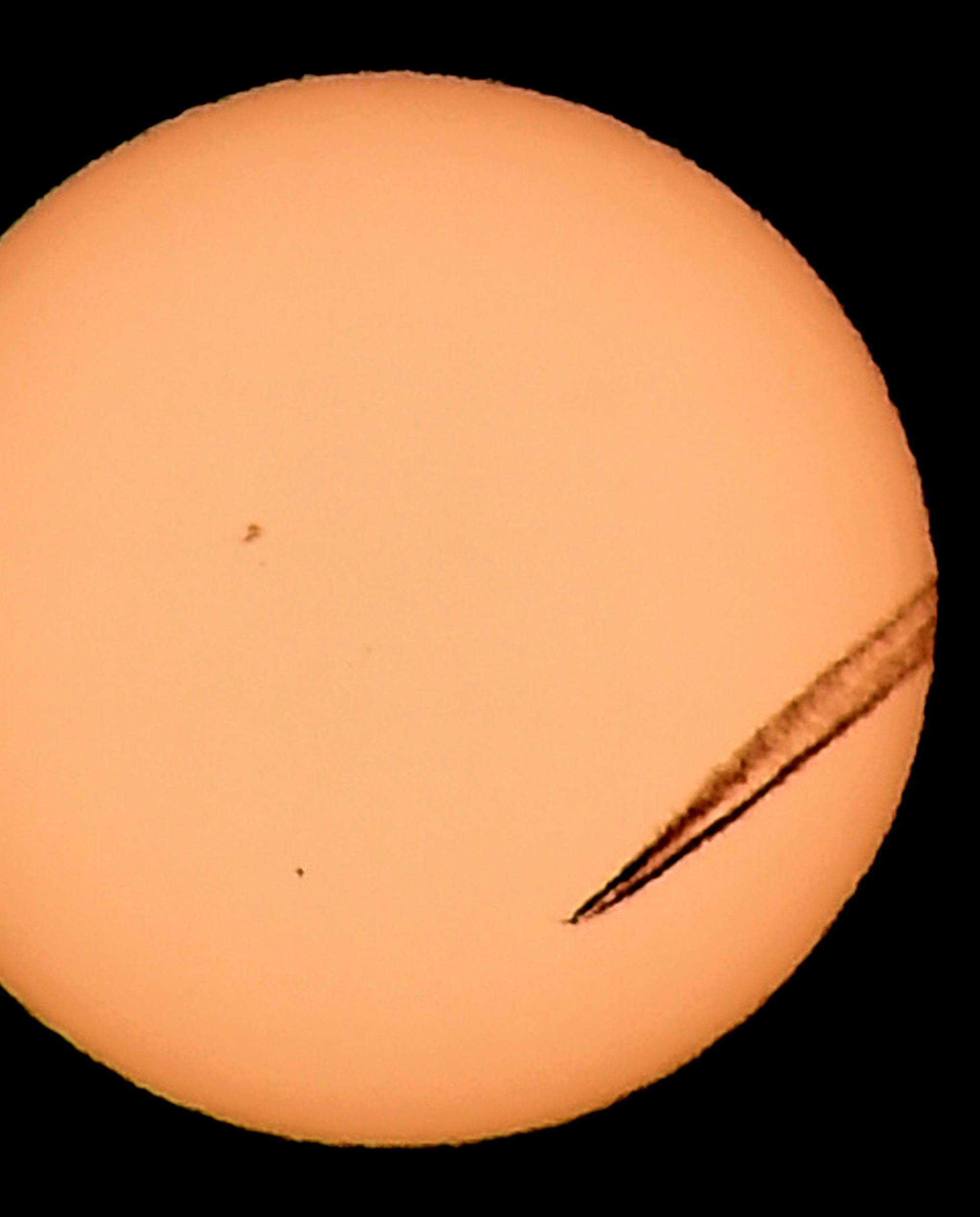 A jet airliner leaves a vapor trail as the planet Mercury is seen, lower left quadrant, transiting across the face of the sun in Las Vegas