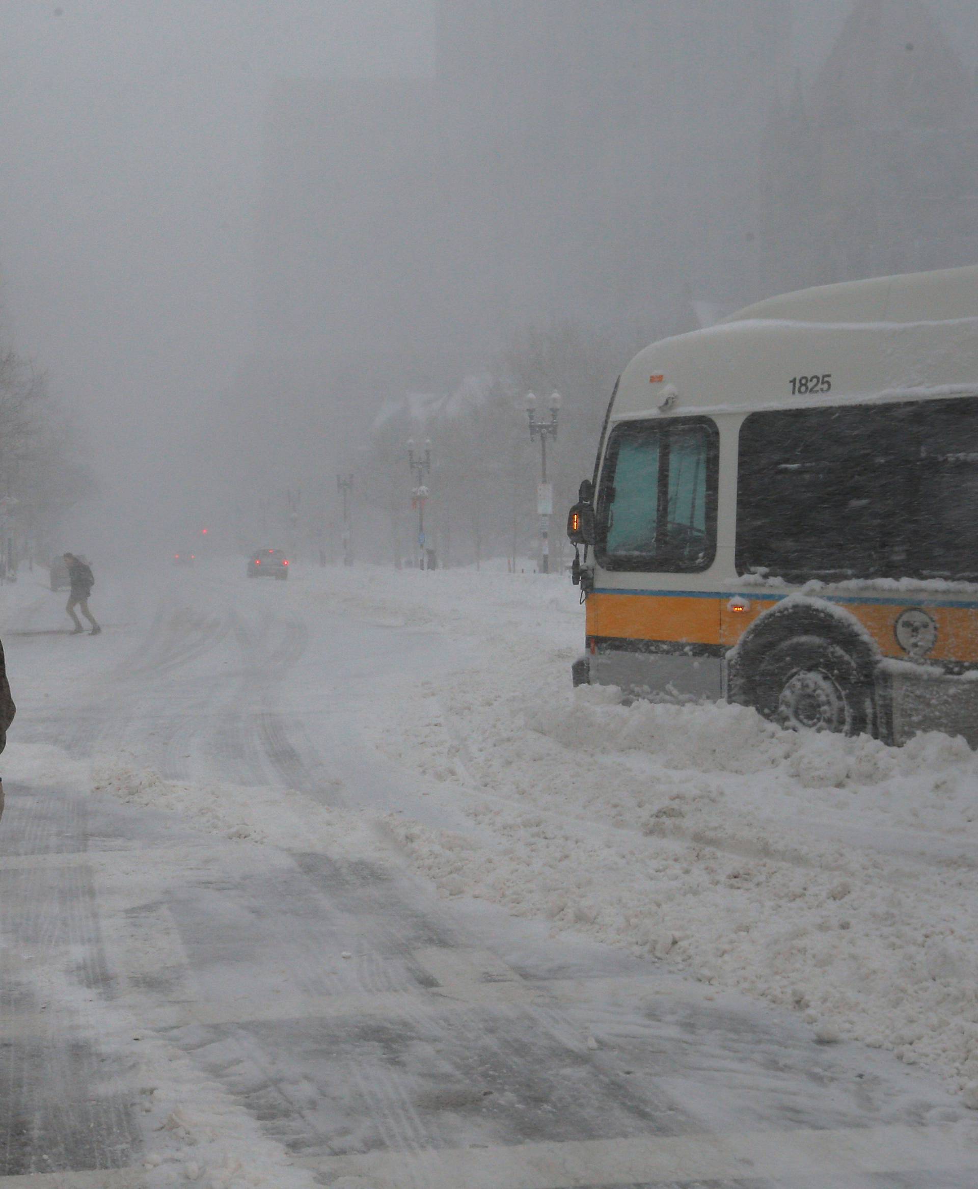 Pedestrians pass a disabled public MBTA bus during Storm Grayson in Boston