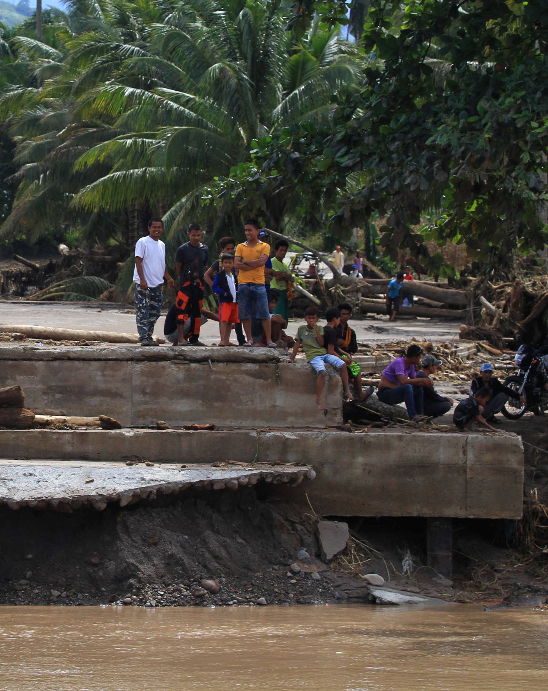 Residents stand on the edge of a destroyed bridge after flash floods in Salvador, Lanao del Norte