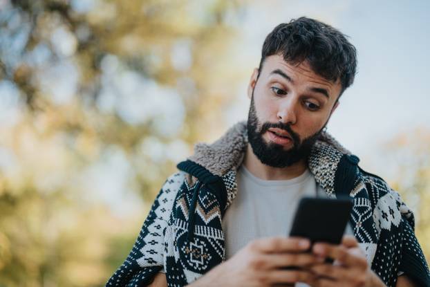 Man outdoors looking surprised at his phone in casual outfit