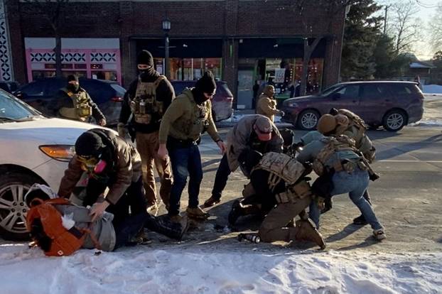 Law enforcement officers kneel next to the body of a man who was shot when federal agents were trying to detain him in Minneapolis