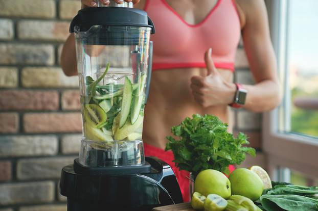 close up of young woman with blender and green vegetables making detox shake or smoothie at home