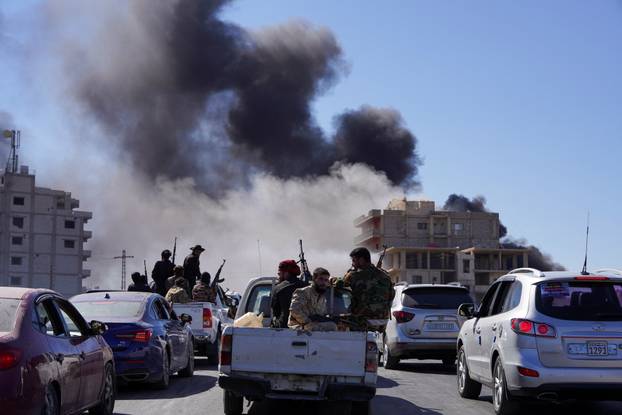 Smoke rises while Syrian security forces sit in the back of a truck, in Sweida