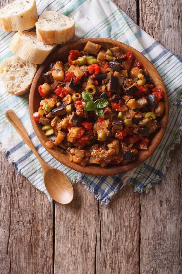 Caponata with aubergines in a wooden plate. vertical top view