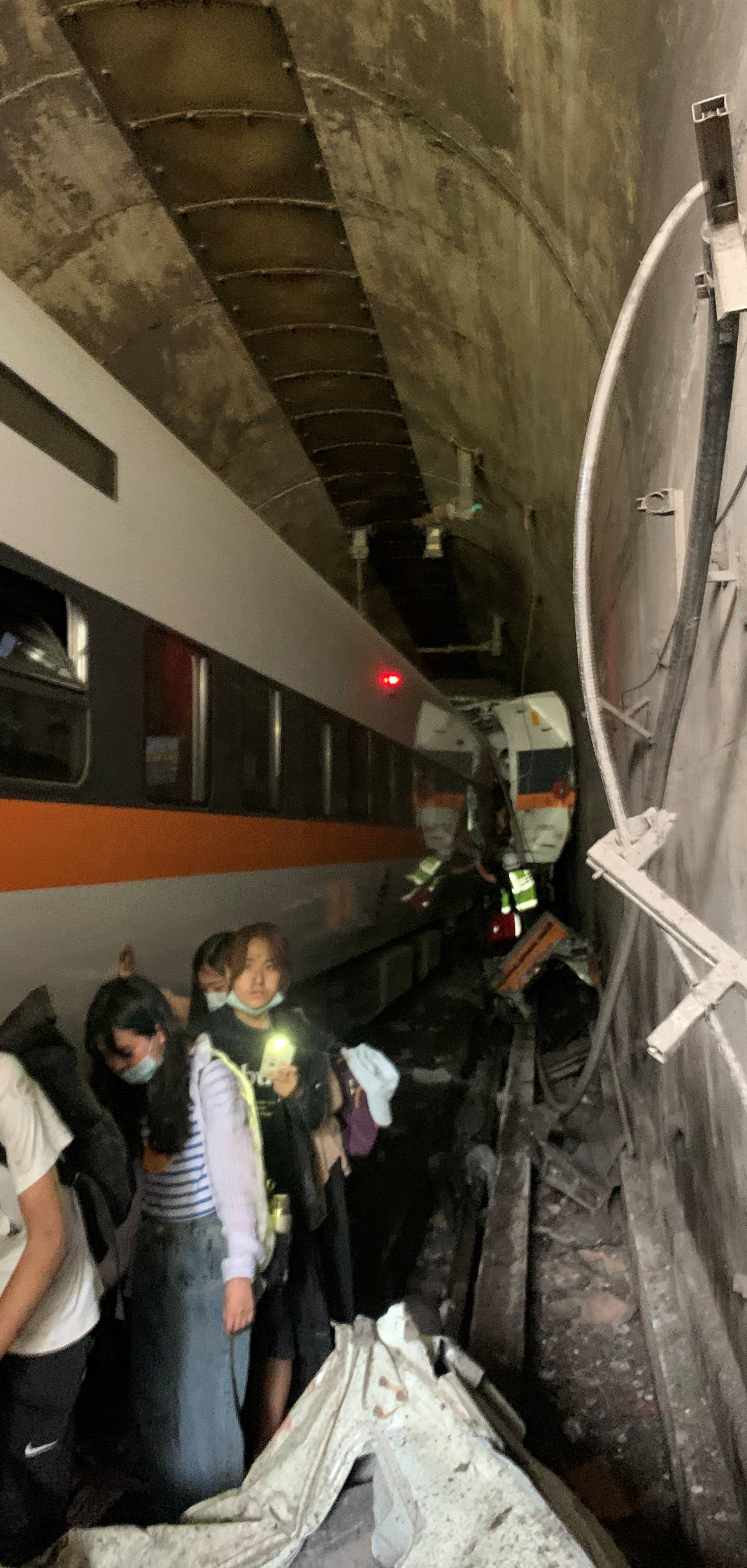 People walk next to a train which derailed in a tunnel north of Hualien