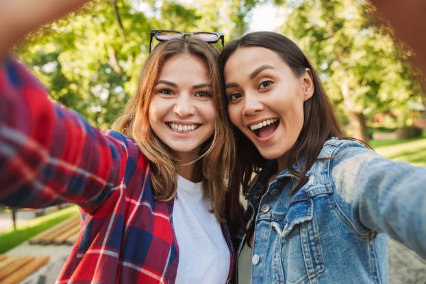 Beautiful ladies students walking in the park take a selfie by mobile phone.