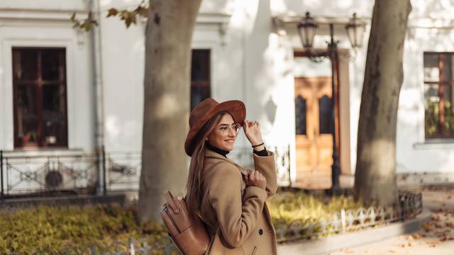 A young woman dressed in a coat and with a backpack is walking in the autumn European city