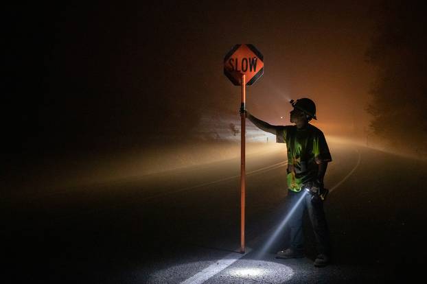 Man holds sign for oncoming traffic as utility workers repair power lines in aftermath of the Obenchain Fire in Eagle Point, Oregon