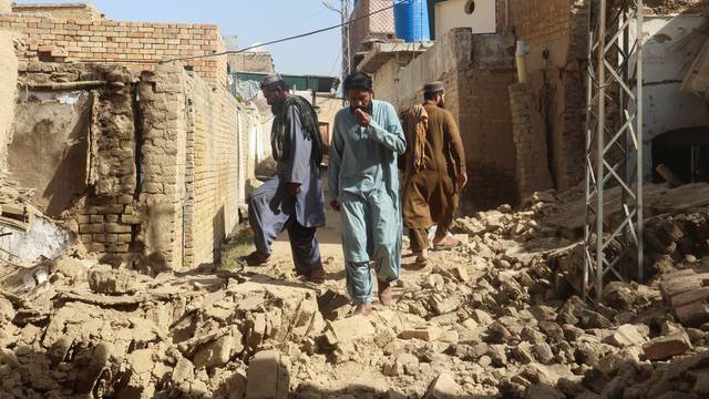 Residents walk amid the rubble of damaged houses along a street following an earthquake in Harnai