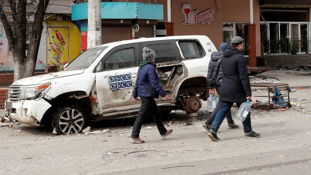 People walk past a damaged OSCE car in Mariupol