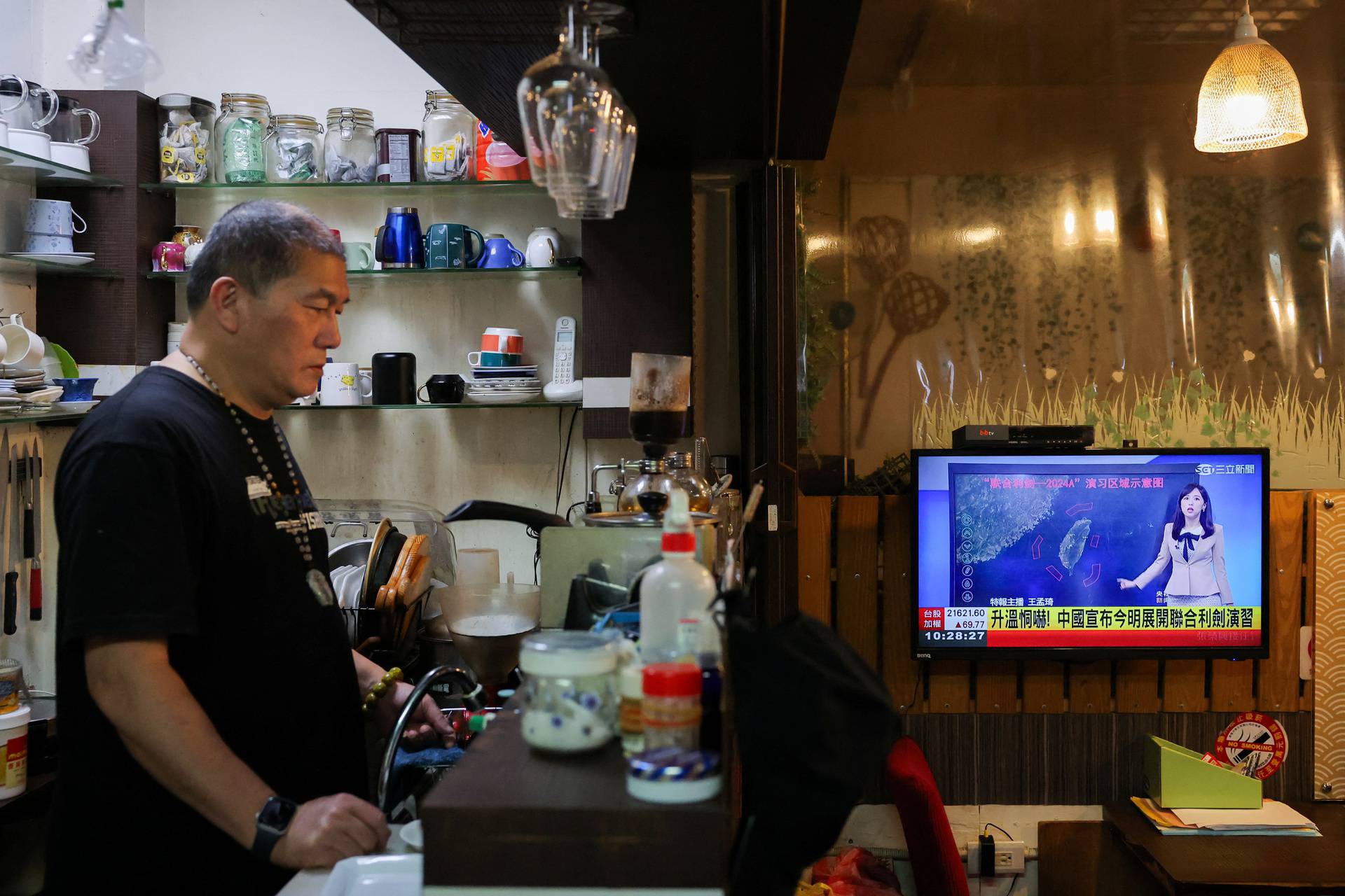 A person stands in a cafe as a news broadcast shows China announcing new military drills around Taiwan, in Keelung