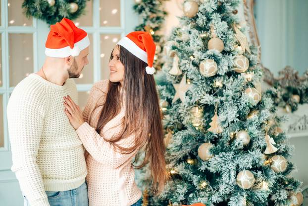 happy couple on Christmas day standing in front of the decorated tree smiling