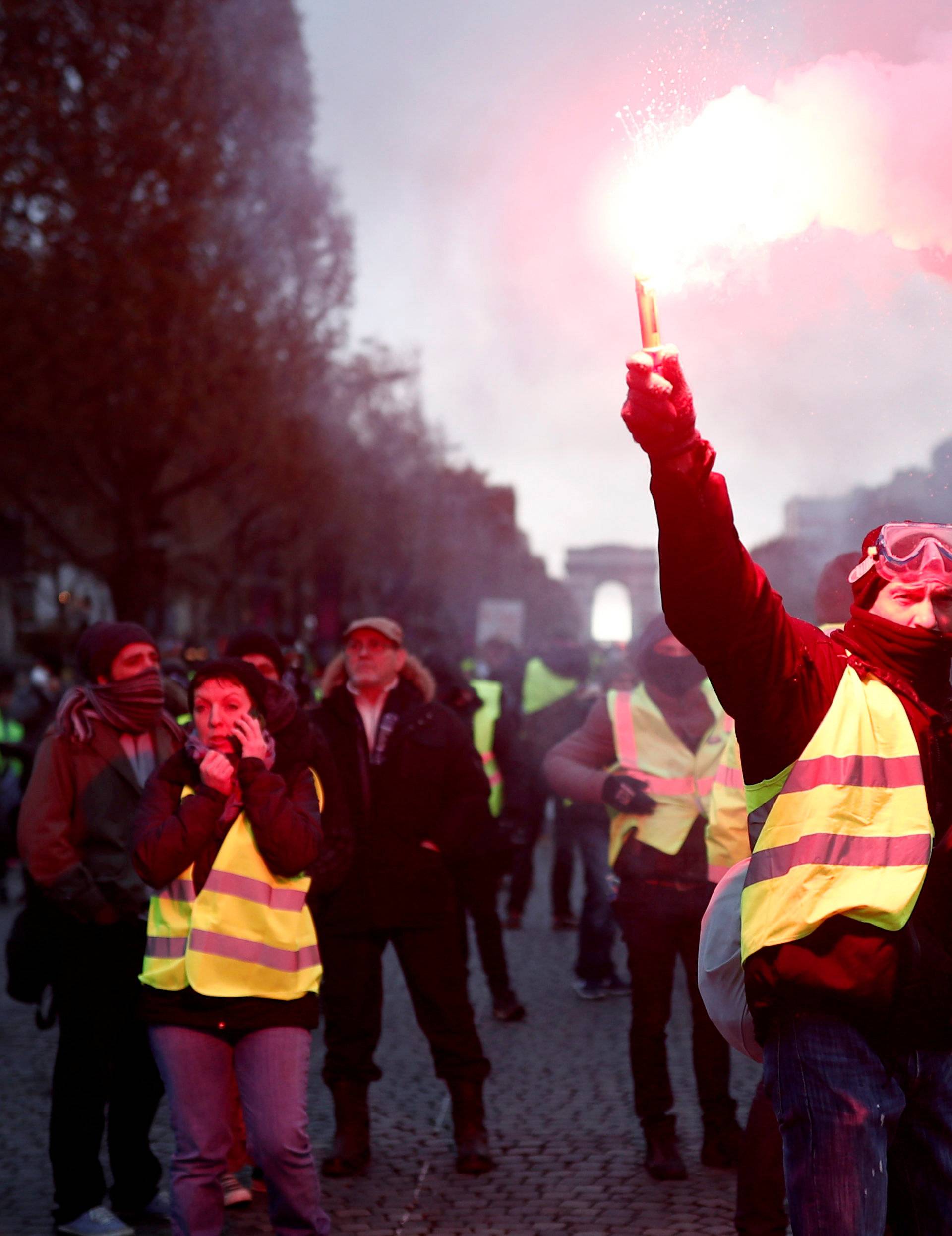 A protester wearing yellow vest, a symbol of a French drivers' protest against higher fuel prices, burns flare on the the Champs-Elysee in Paris