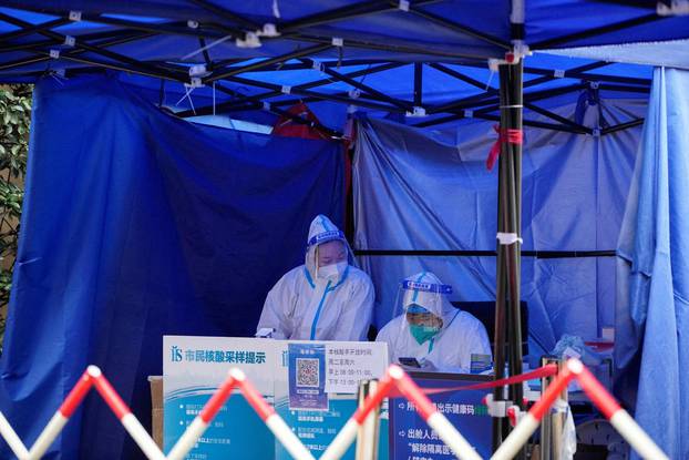 FILE PHOTO: Workers in protective suits wait for people at a nucleic acid testing site in Shanghai