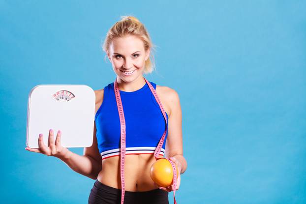Žena drži vagu, metar i naranču - gubitak težine