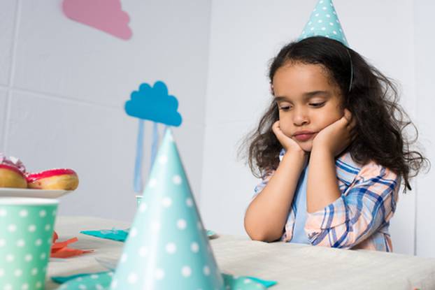 upset little african american girl sitting alone at birthday table
