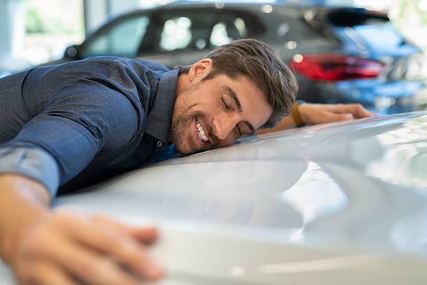 Happy,Young,Man,Hugging,His,New,Car,In,Showroom.,Satisfied
