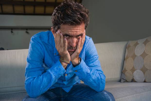 young attractive and handsome sad latin man sitting tired and depressed at home sofa couch feeling overwhelmed and worried suffering depression crisis and anxiety