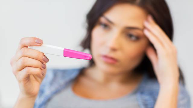 close up of sad woman with home pregnancy test
