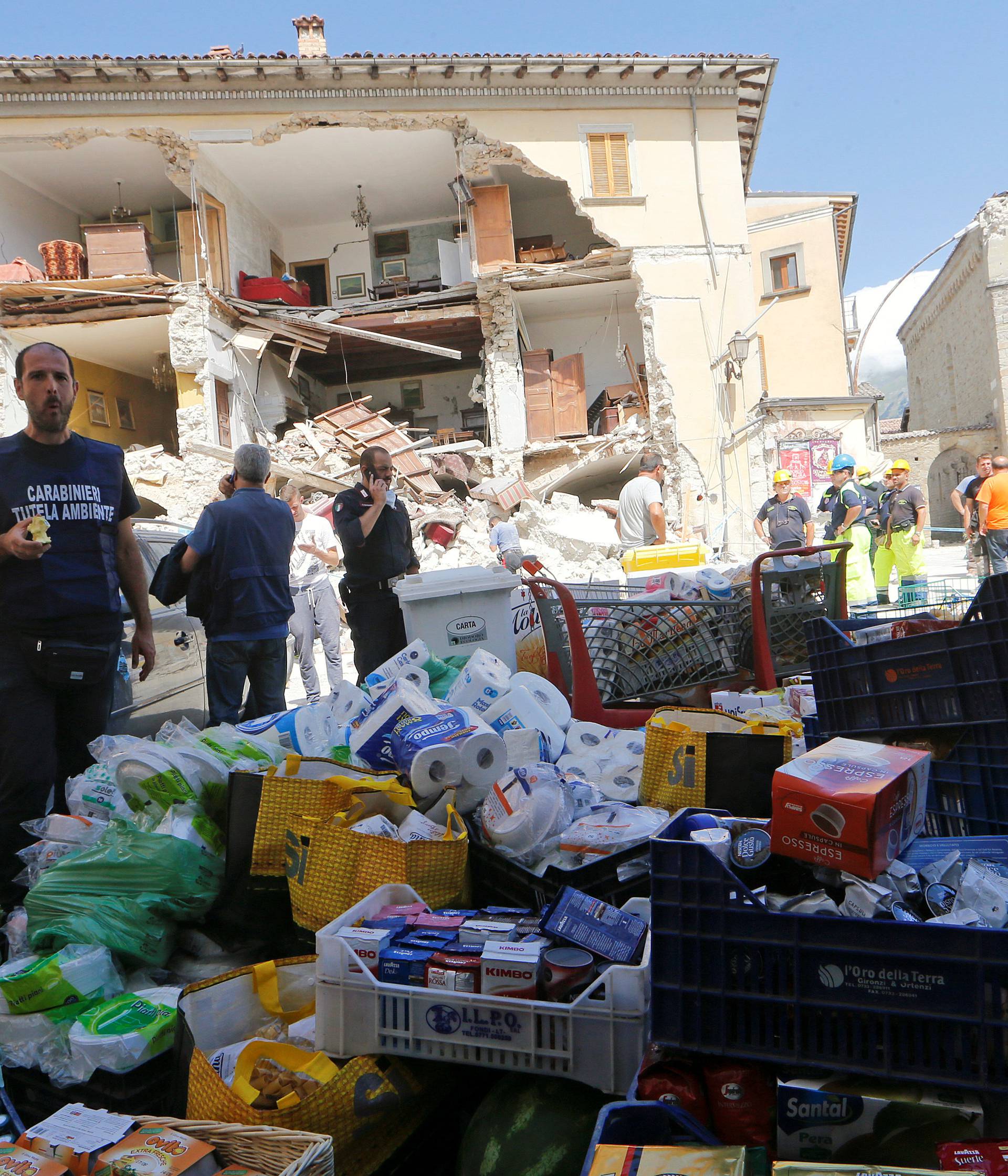 Rescuers prepare food and basic necessities in front of a partially collapsed building following an earthquake in Amatrice