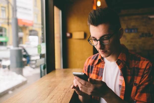 Close up on the hands of a young handsome man using  smartphone, tapping the screen - technology, social network, communication concept