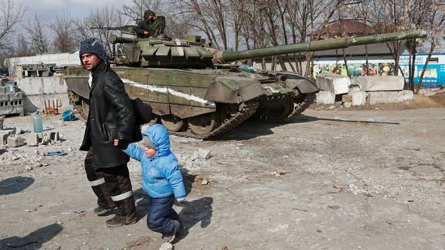 A local resident walks with a child past a tank of pro-Russian troops in the besieged city of Mariupol