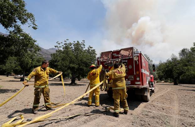 Firefighters prepare hoses on the back of their brush rig as a smoke column grows from the Ranch Fire north of Upper Lake, California