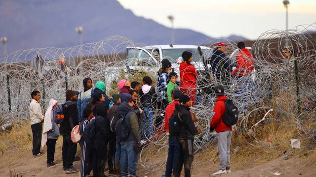 Migrants seeking asylum try to cross a razor wire fence into the United States, as seen from Ciudad Juarez