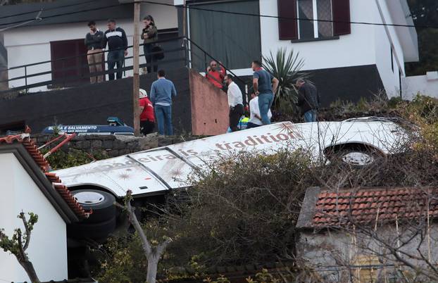 People stand next to the wreckage of a bus after an accident in Canico