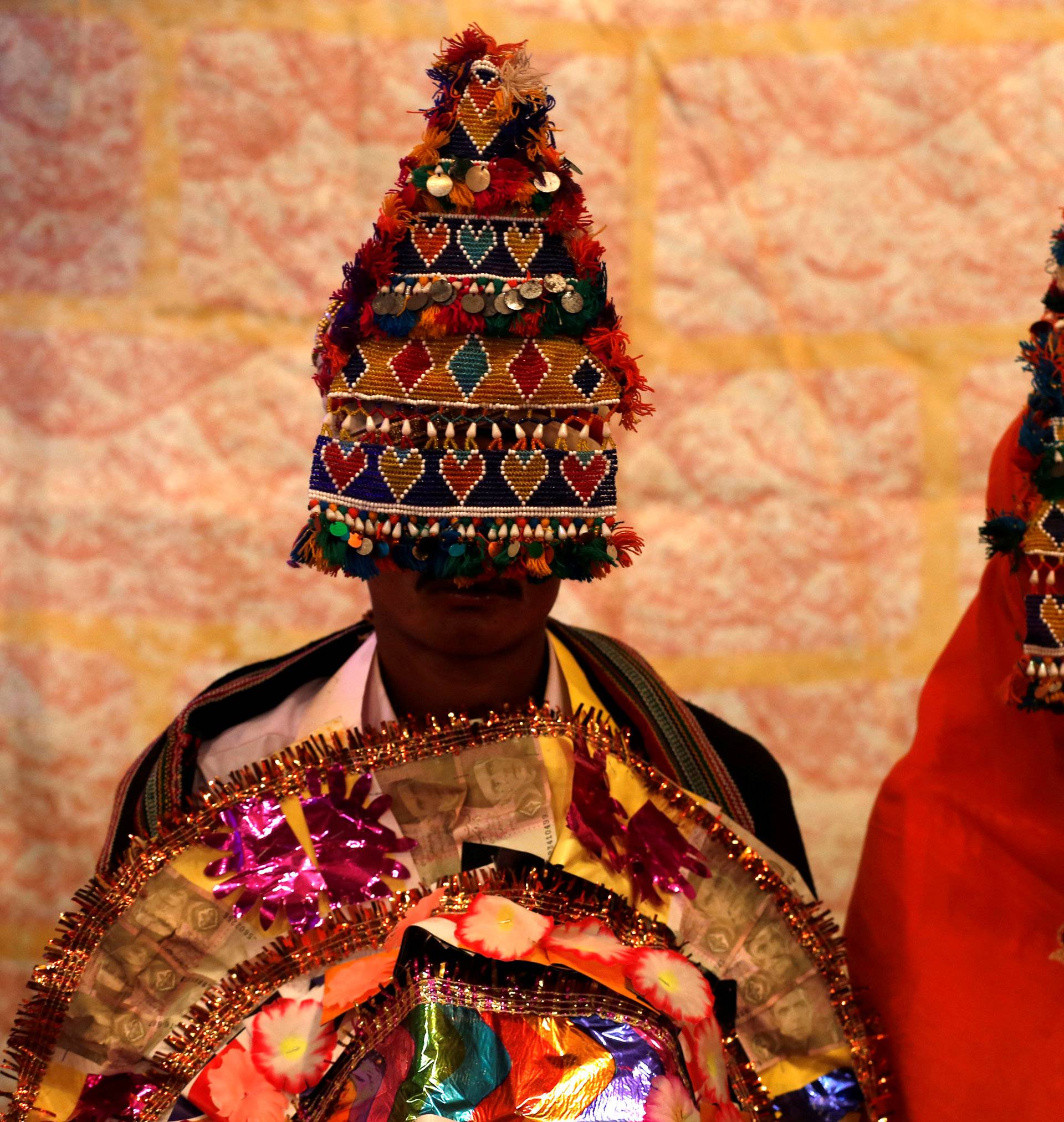 A bride and groom wearing traditional handmade garlands wait for their wedding to start during a mass marriage ceremony in Karachi