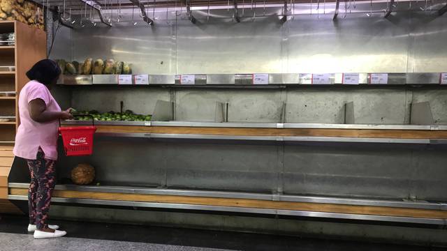 A woman selects lemons from partially empty shelves at the fruits and vegetables area in a supermarket in Caracas