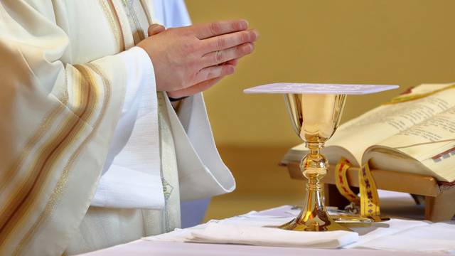 Chalice on the altar and priest celebrating mass in the background and empty space for text
