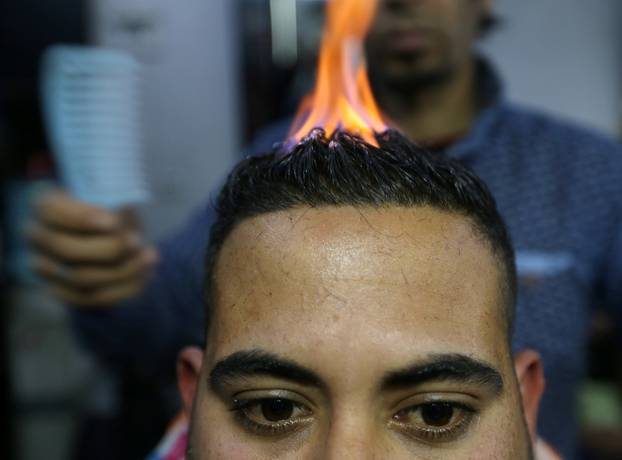 Palestinian barber Ramadan Odwan styles and straightens the hair of a customer with fire at his salon in Rafah, in the southern Gaza Strip