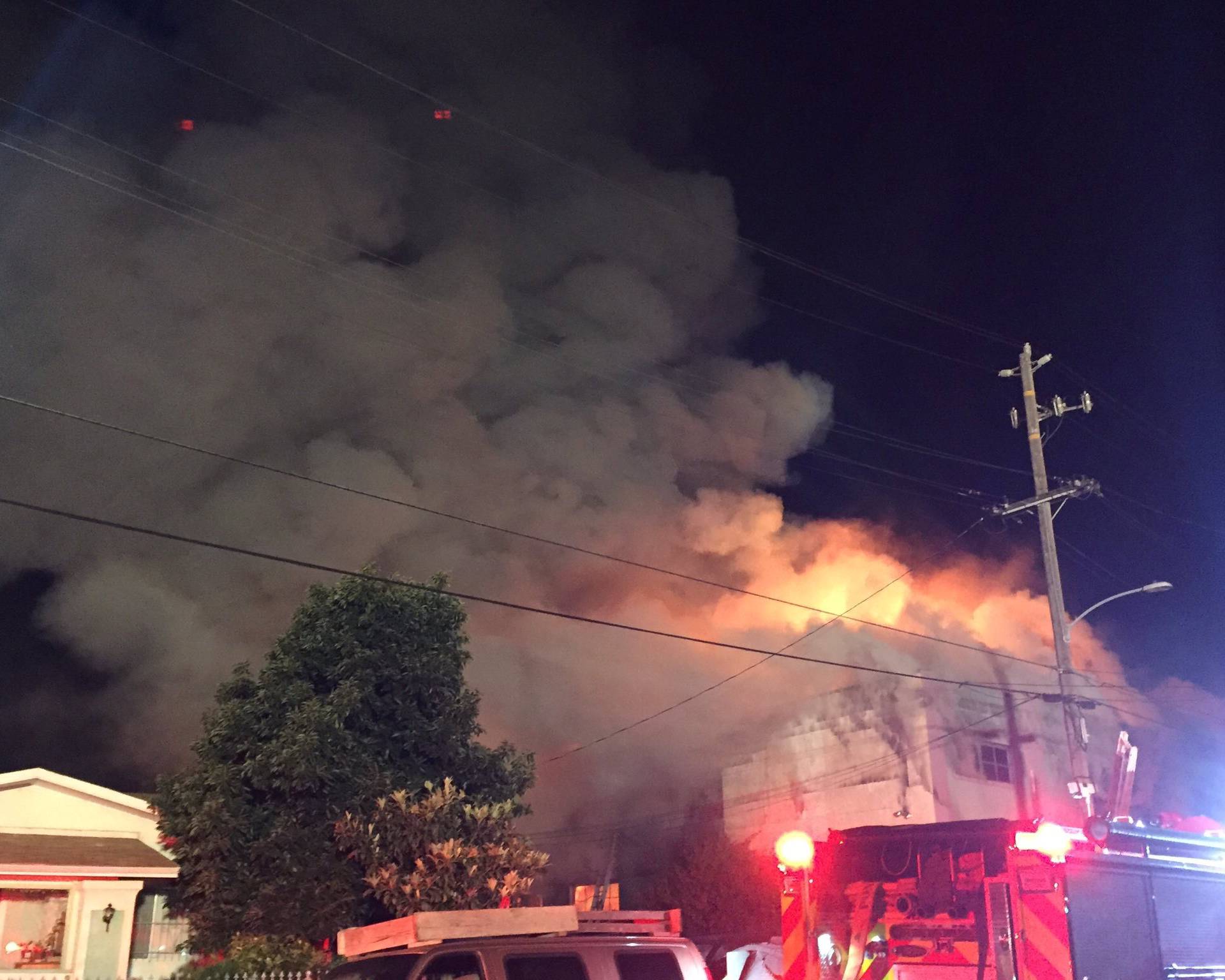 Flames rise from the top of a warehouse, which caught fire during a dance party in Oakland