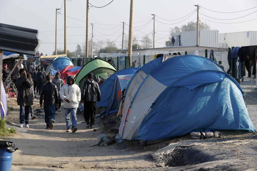 Migrants walk in an alley near tents and makeshift shelters on the eve of the evacuation and dismantlement of the camp called the "Jungle" in Calais