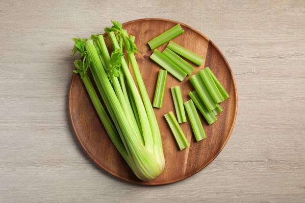 Board with fresh cut celery stalks and bunch on wooden table, to