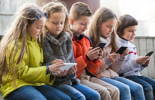 Ordinary,Kids,Sitting,With,Mobile,Devices,In,Street