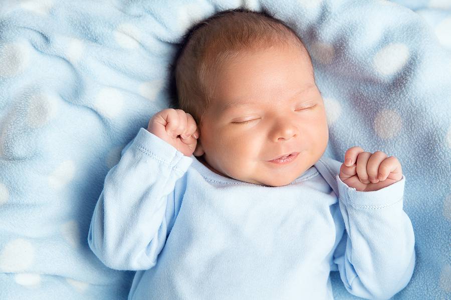 Newborn Baby Sleeping Smiling. Cute Infant Child In Wrap Bodysui